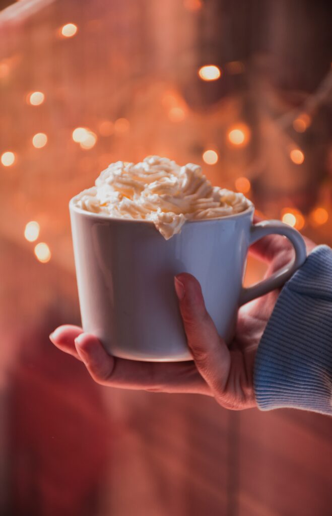 a cosy outstretched hand holds a warm cup of coffee topped with whipped cream and sprinkled spice